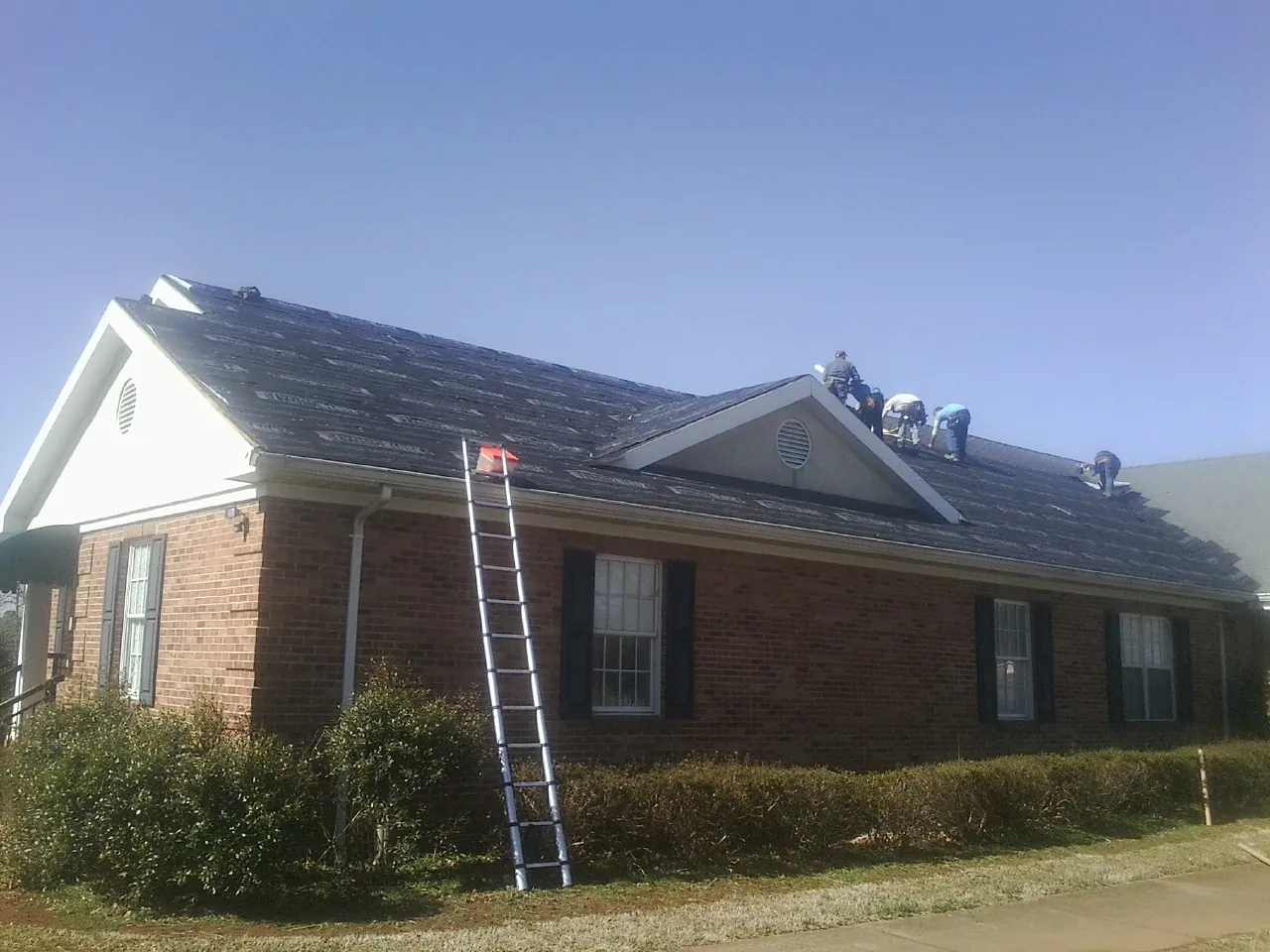 Crew tearing shingles off a brick ranch roof with a ladder set — Metal Roof Repair work by our crew in New Alexandria