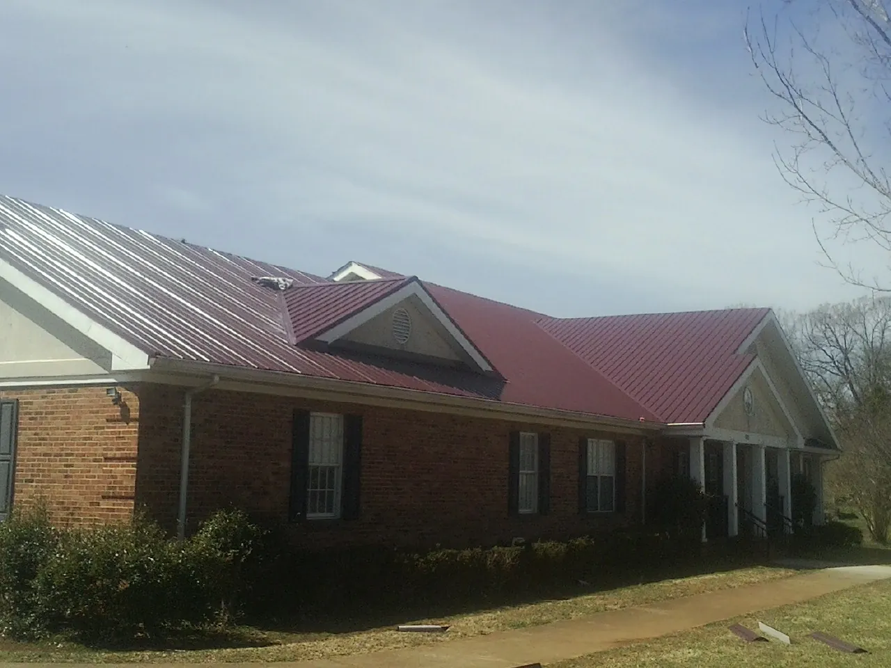 Red metal roof with gabled entries on a long brick building, from a Hail Damage Roof Repair job in New Alexandria