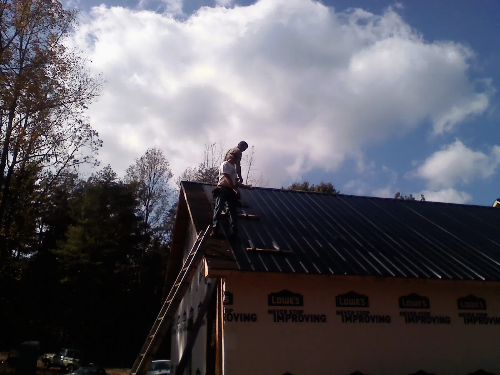 Roofer fastening dark metal panels high against a cloudy sky, from a Roof Inspection job in New Alexandria