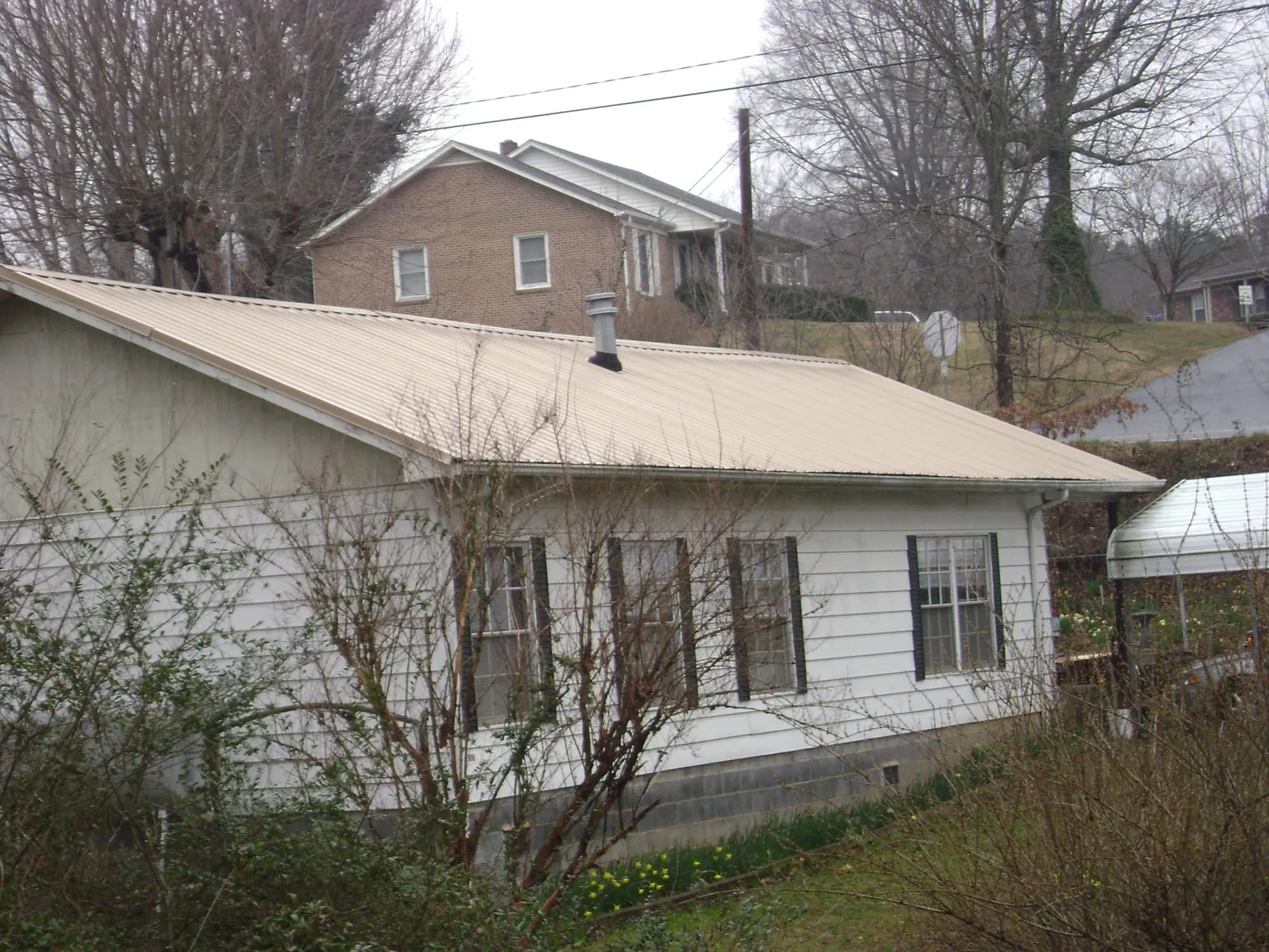 Tan metal roof on a white sided house set into a hillside — Commercial Roofing by Roofing Brothers in New Alexandria