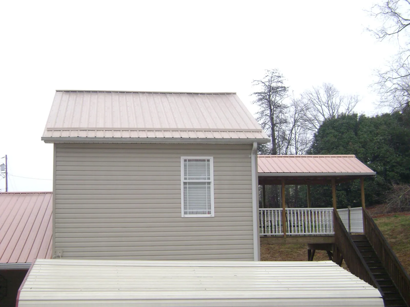 Tan metal roofs on a two story addition and attached porch, from a Roof Replacement job in New Alexandria